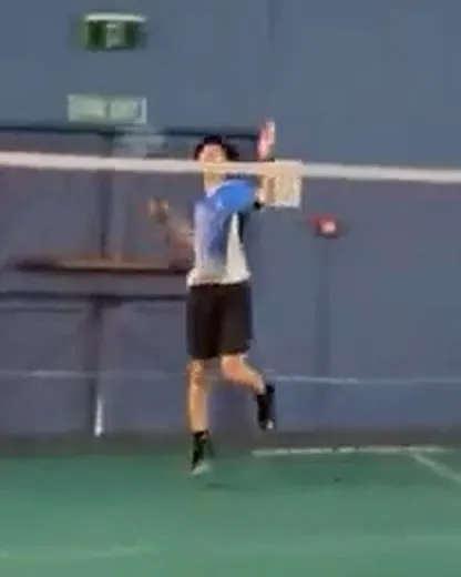 Oliver mid-jump playing a smash on a badminton court